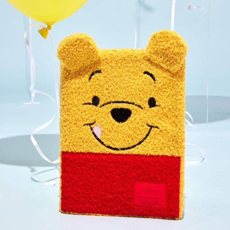 The Loungefly Winnie the Pooh Cosplay Plush Refillable Stationery Journal sitting upright against a pale blue background with balloons behind it